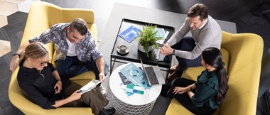 Two men and two women sat on yellow sofas with a table in the middle