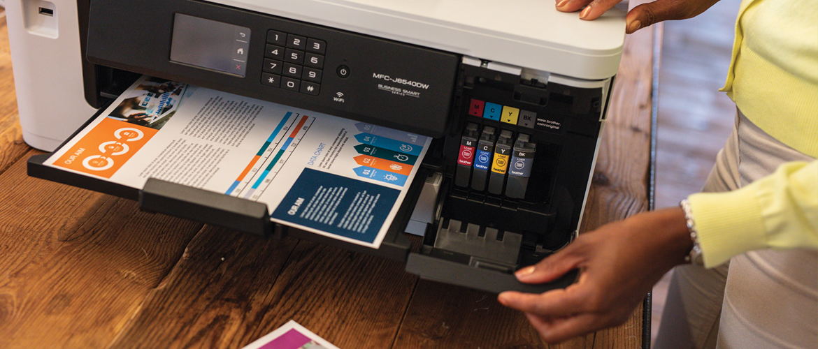 A woman stood next to a print out on a printer showing the 4 CMYK supplies