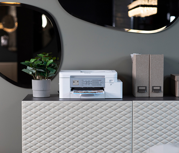 White inkjet printer alongside a plant and two files on a sideboard with a mirror behind