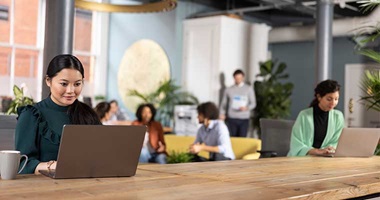 Busy office, lots of people working on laptops, plants, printers