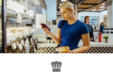 Woman with blond hair wearing blue tshirt looking at a juice bottle holding sandwich